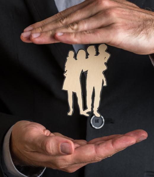 Closeup of businessman or insurance agent making protecting gesture around a paper cut silhouette of a family. Conceptual of safety and life insurance.